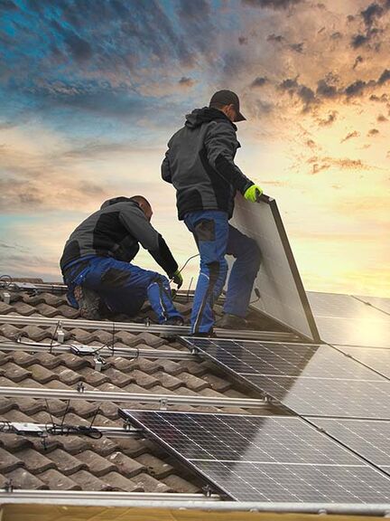Zwei Personen installieren Solarpaneele auf einem Ziegeldach bei Sonnenuntergang. Zwei Personen installieren Solarpaneele auf einem Ziegeldach bei Sonnenuntergang.